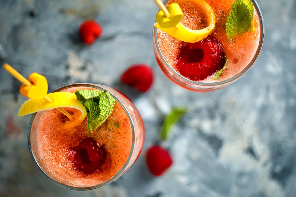 Raspberry twist cocktail in two champagne glasses with a lemon twist and mint leaf.