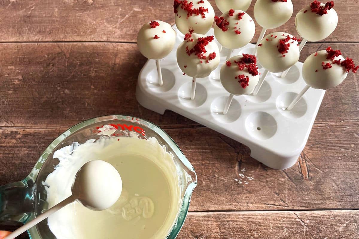 Red velvet cake pops getting dipped and decorated in stand.