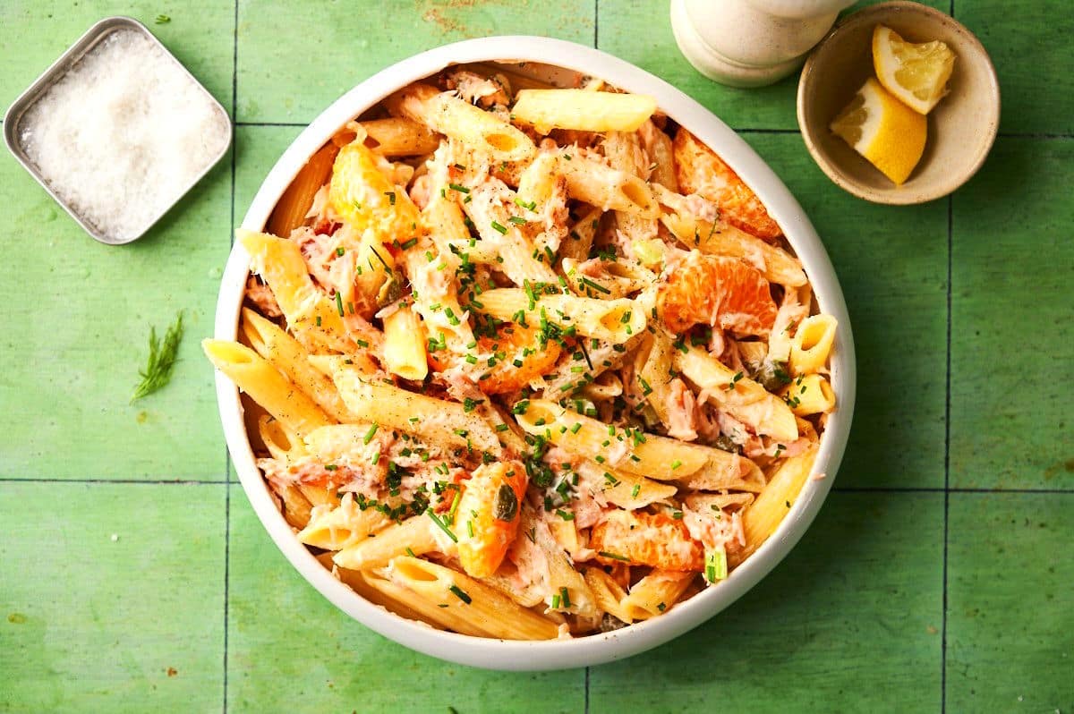 Smoked salmon pasta salad in bowl with fresh lemon, salt and pepper on the side.