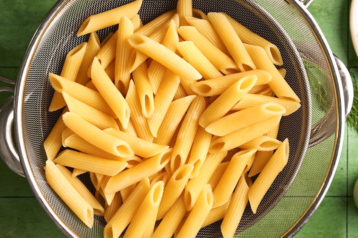 Penne pasta draining in mesh strainer.