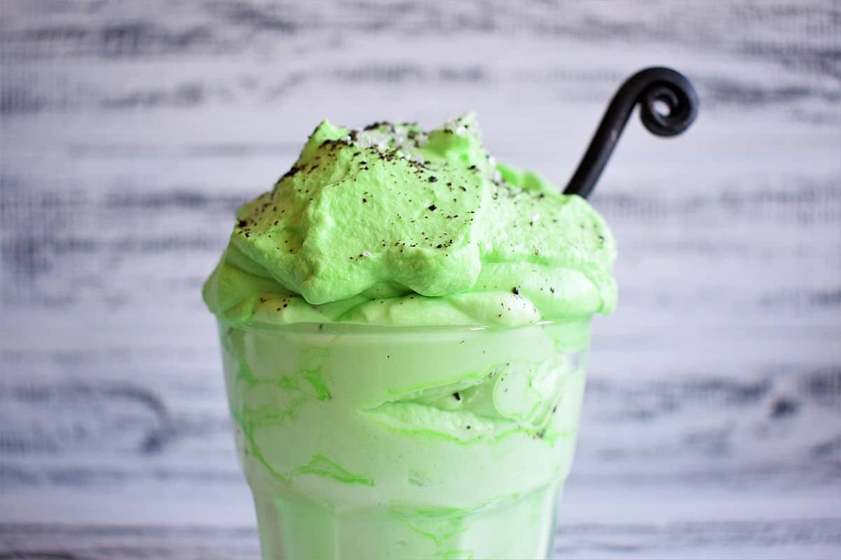 Green peppermint whipped cream with sprinkles and black curled spoon in glass.