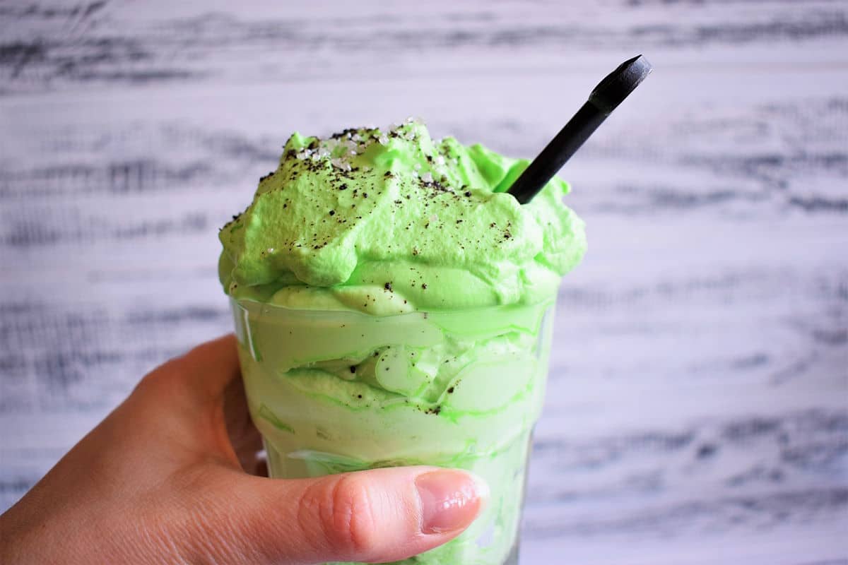 Green peppermint whipped cream in glass in hand.