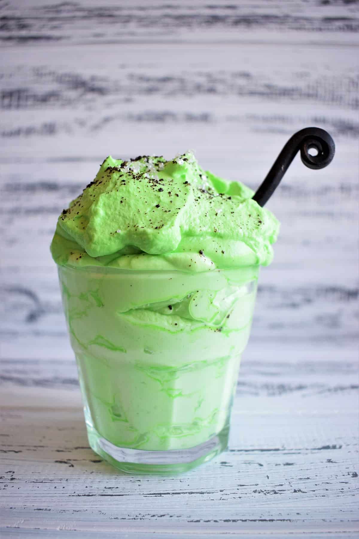 Green peppermint whipped cream with black spoon in glass.