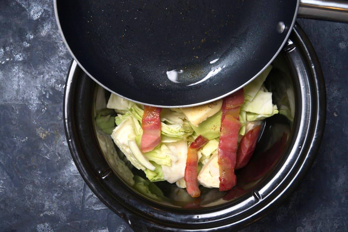 Bacon grease in pan pouring into slow cooker with cabbage and bacon.