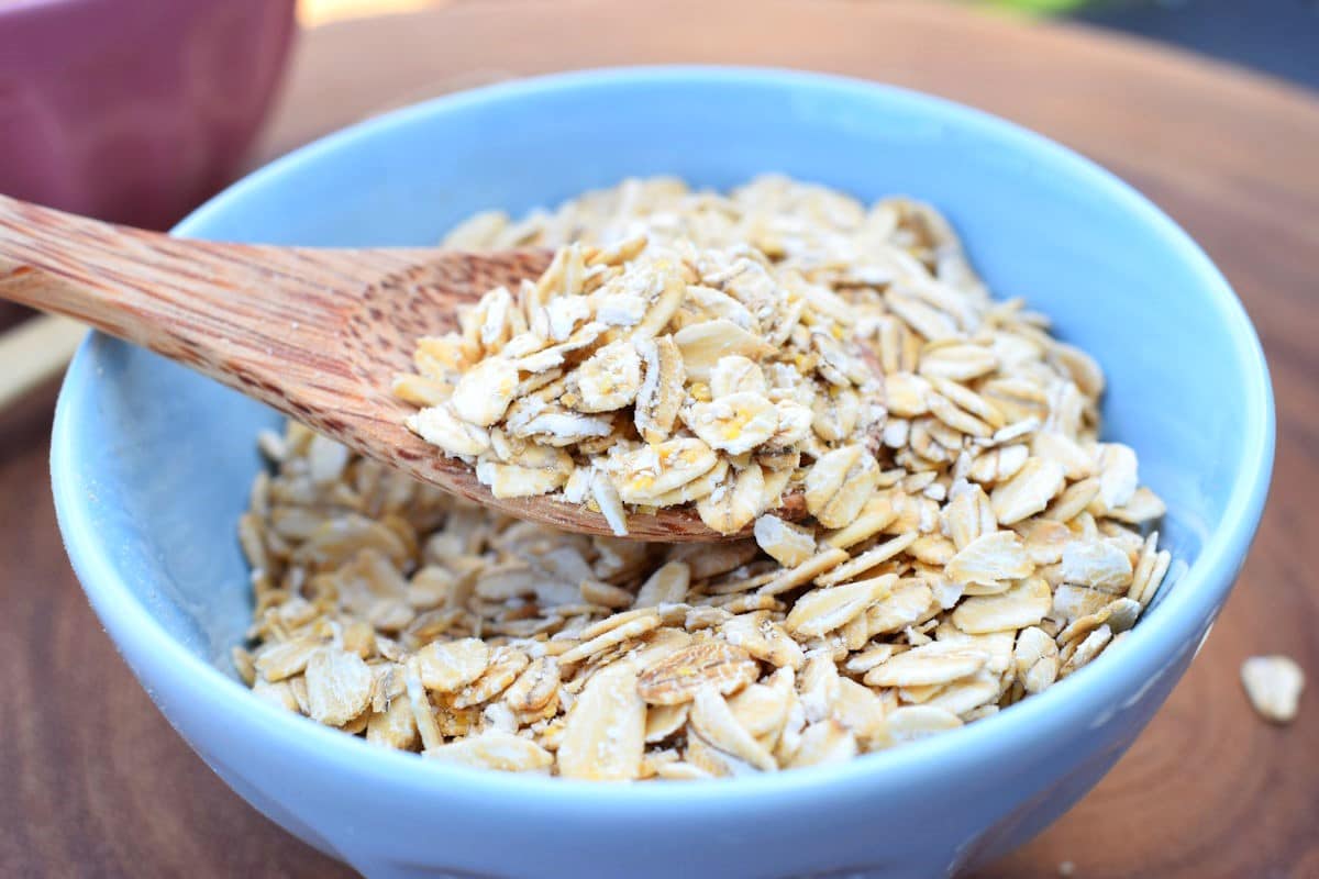 Rolled oats in blue bowl with wooden spoon.