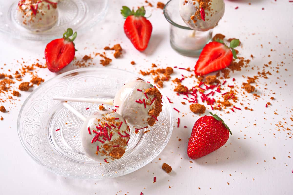 Strawberry shortcake cake pops on clear glass plate surrounded by fresh strawberries.