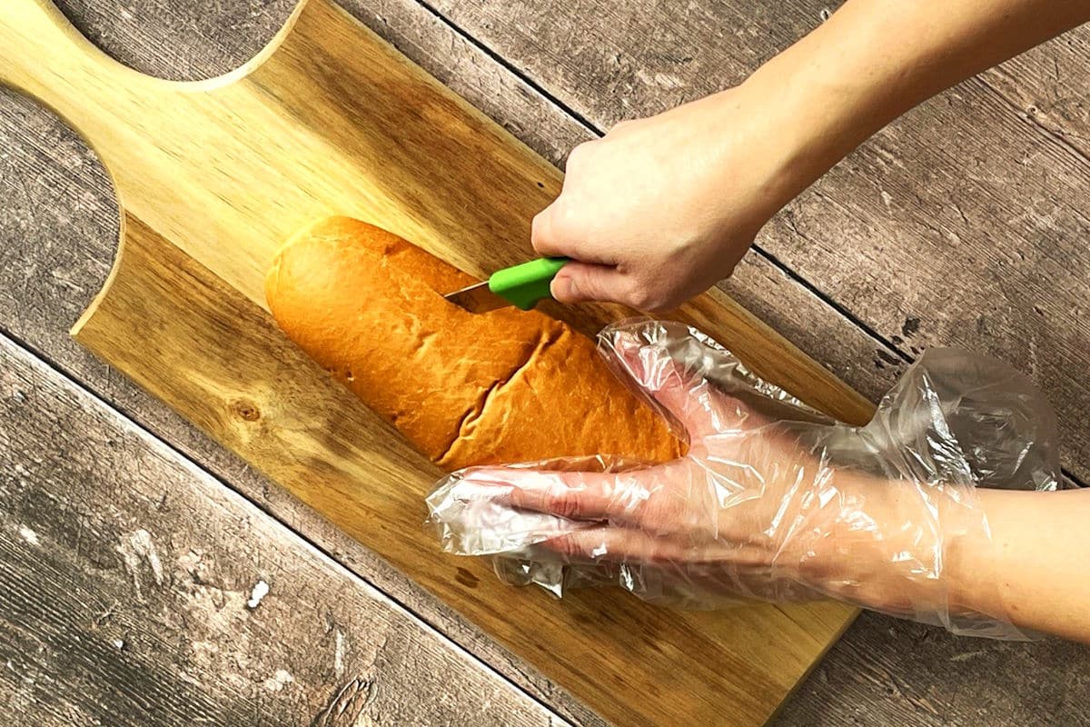 Sub bun getting sliced with hinge cut on cutting board.