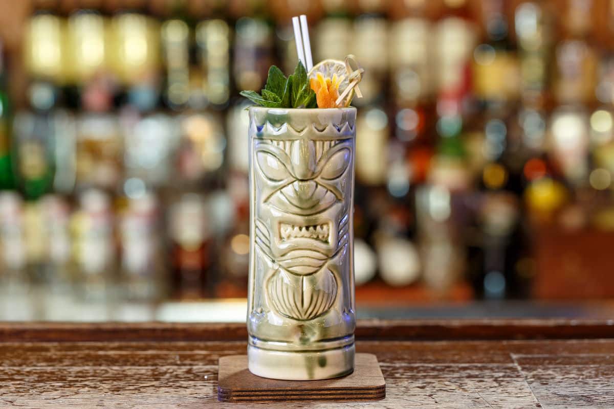 An exotic cocktail in a tiki glass stands on a wooden bar counter in a pub or restaurant.