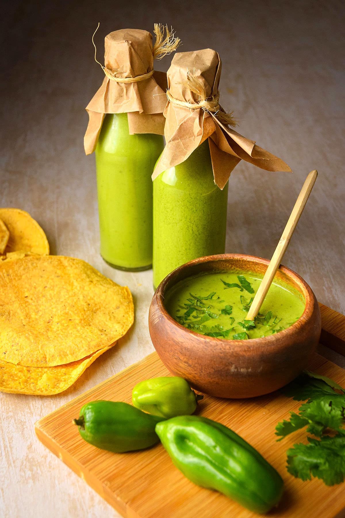 Tomatillo hot sauce in small wooden bowl and hot sauce bottles.