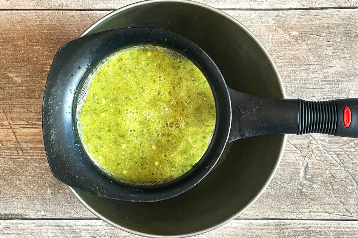 Tomatillo hot sauce straining through fine mesh strainer.