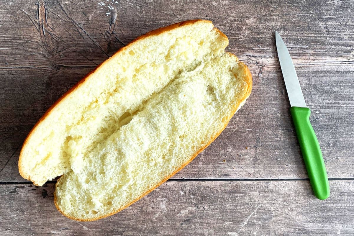 Sub bun sliced in half and opened up with small green knife.