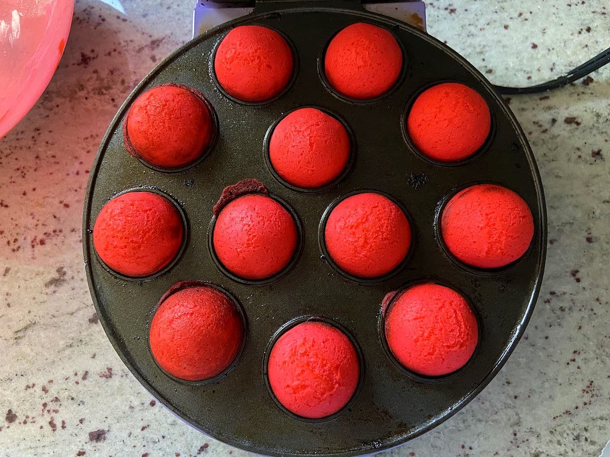 Red cake balls in cake pop maker on countertop.