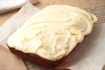 Red velvet sheet cake with cream cheese frosting on baking rack.