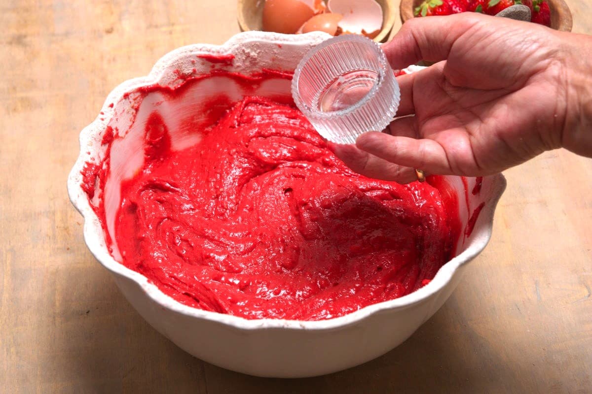 Red velvet cake batter in bowl with small jar of vinegar.