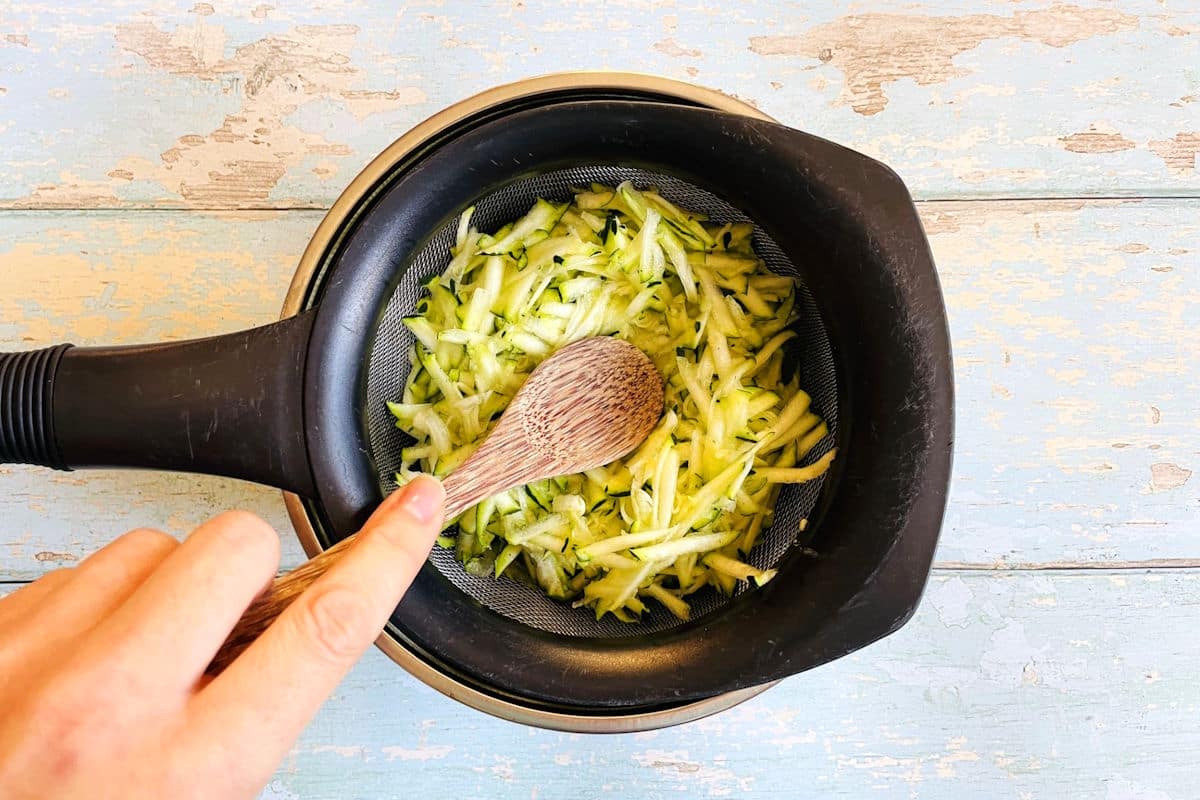 Shredded zucchini in mesh strainer.