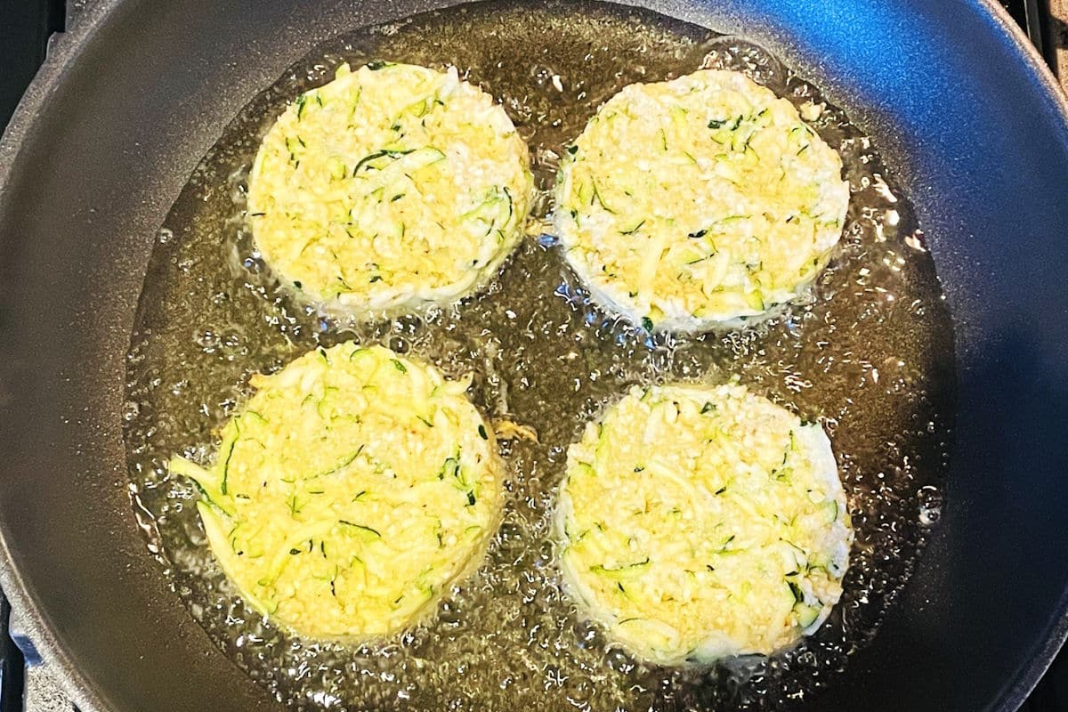 Zucchini crab cakes frying in pan with hot oil.
