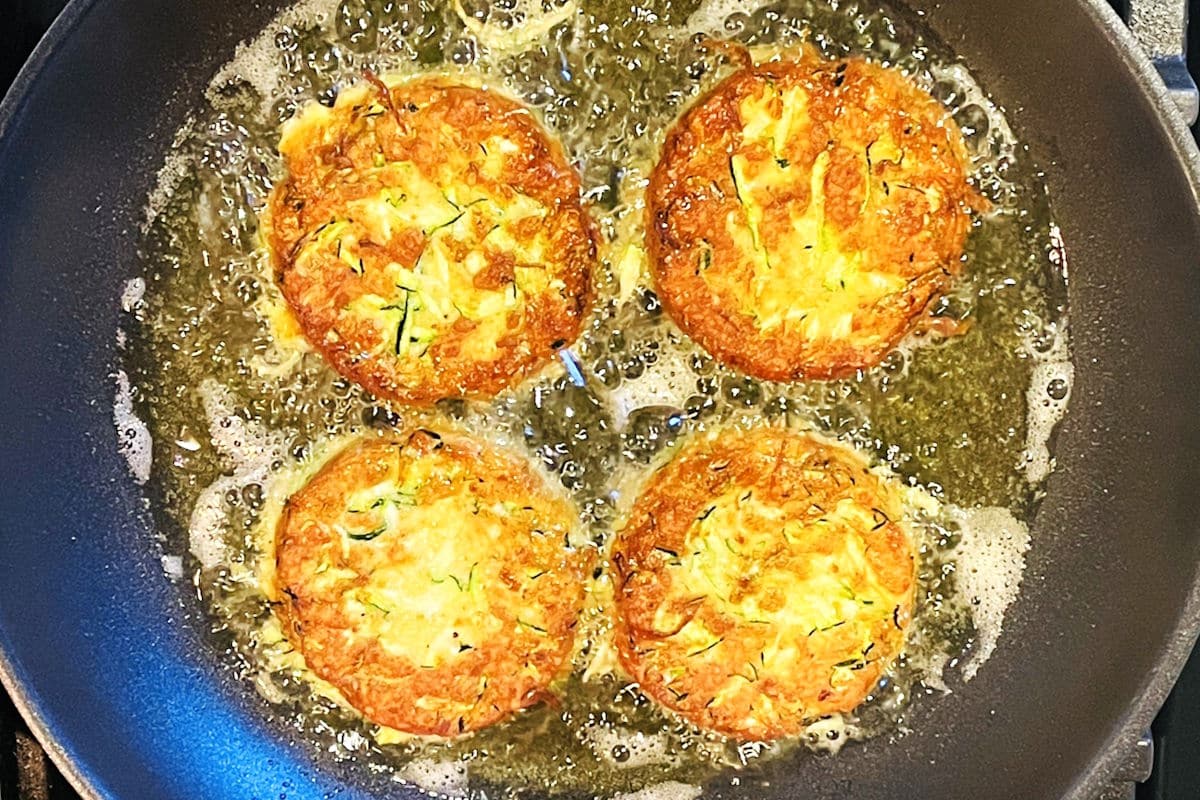 Golden zucchini crab cakes in pan with hot oil.