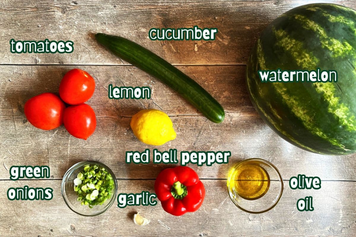 Watermelon gazpacho ingredients labeled on wooden background.