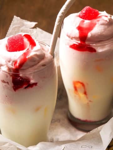 Whipped strawberry milk in 2 glasses with paper straws.